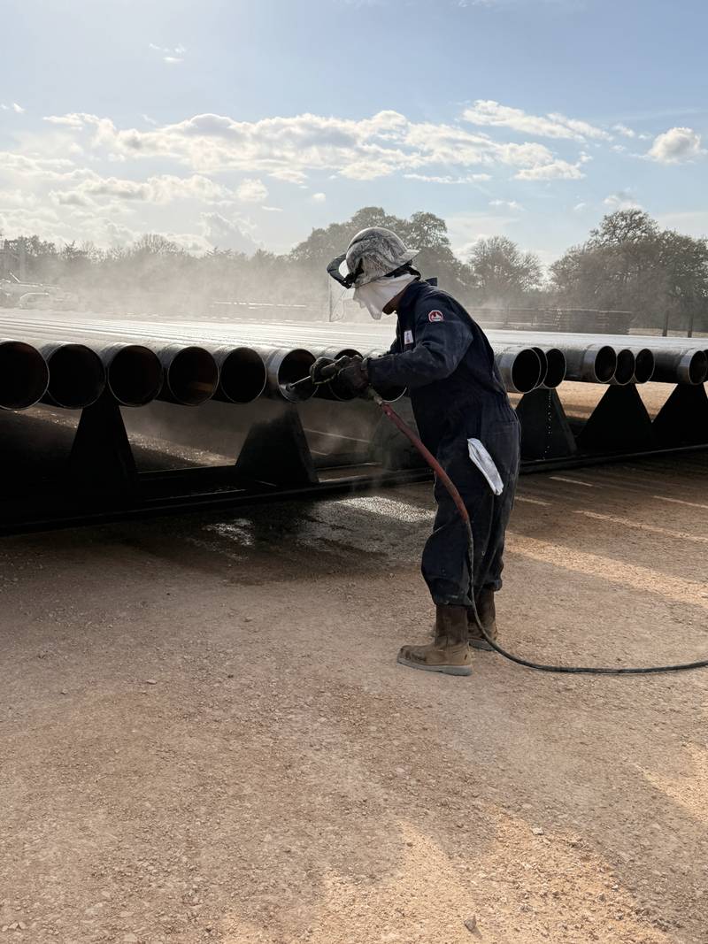 An A.E. & Sons crew member in a face shield, hard hat and coveralls pressure-washing casing on the rack.