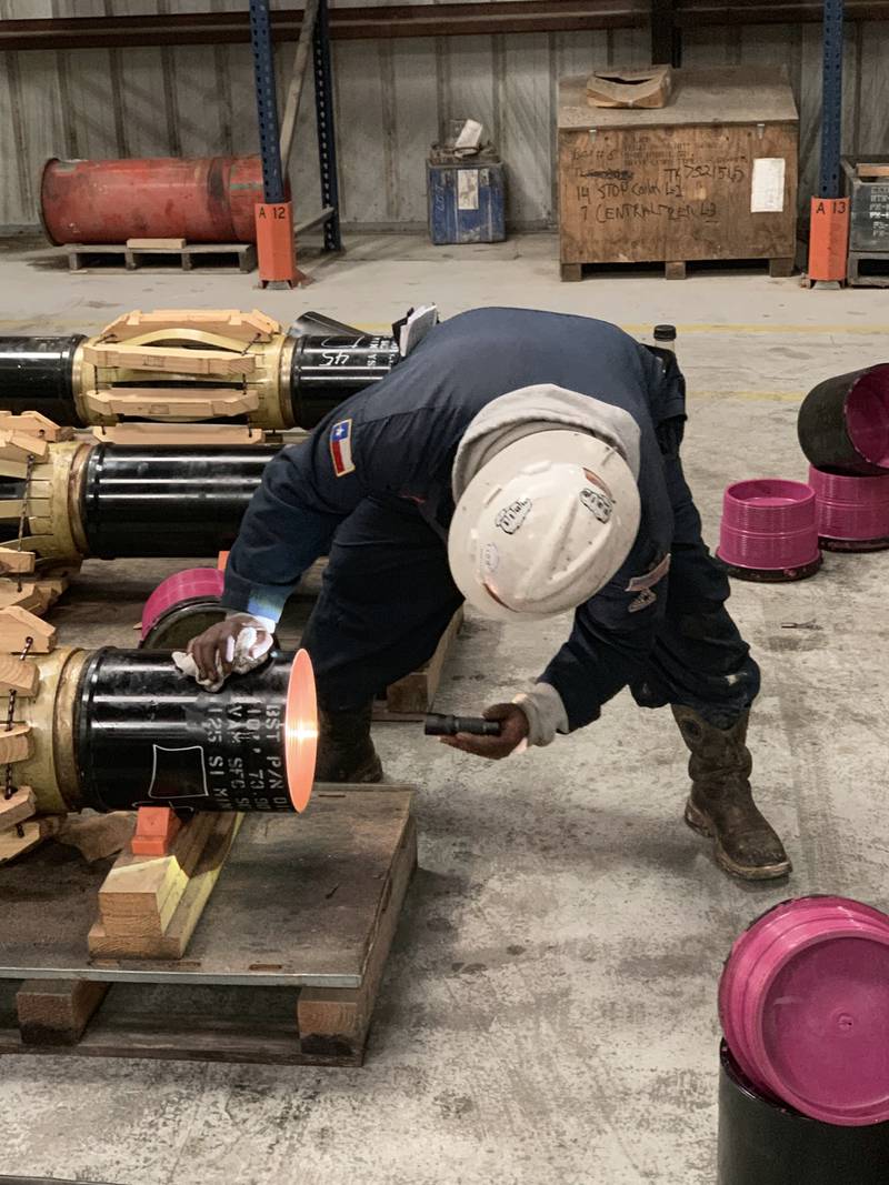 An A.E. & Sons inspector in a hard hat and gloves checks the box end of a premium connection with a flashlight.